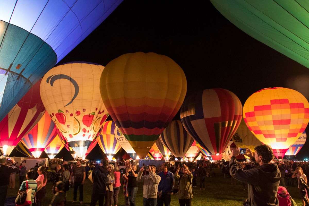 Hot air balloons glowing at night during Balloon Fiesta's evening Balloon Glow, surrounded by a crowd